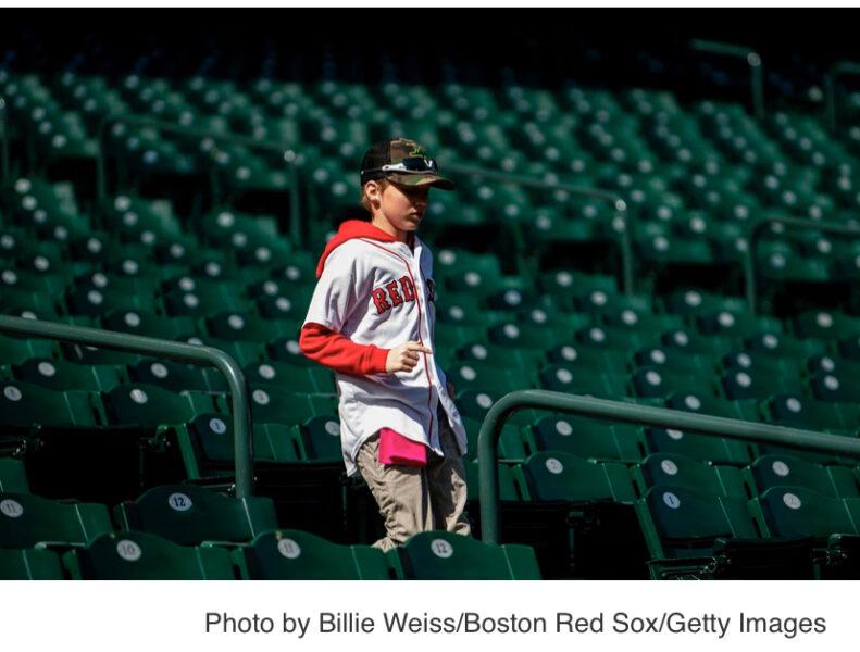 A young child in a Red Sox jersey walks alone in the stands.